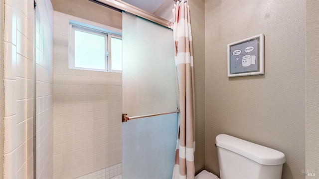 bathroom featuring toilet, tiled shower, and a textured wall