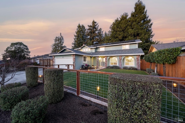 traditional-style home with a shingled roof, a fenced front yard, an attached garage, and a lawn