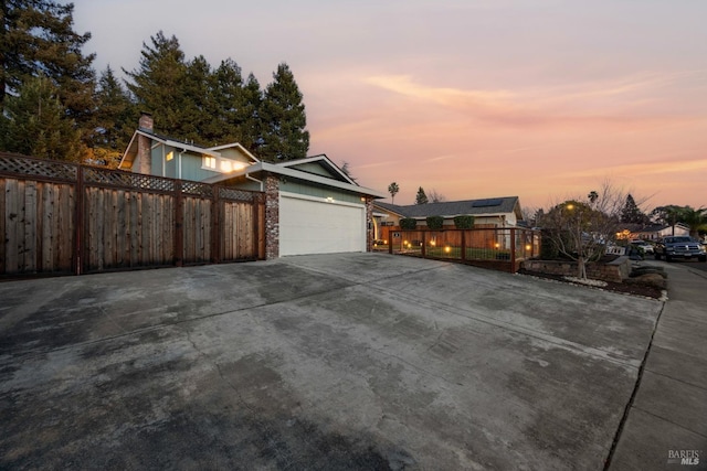 property exterior at dusk featuring fence, driveway, and an attached garage