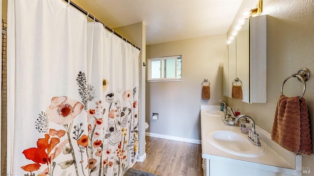 full bathroom with double vanity, baseboards, a sink, and wood finished floors