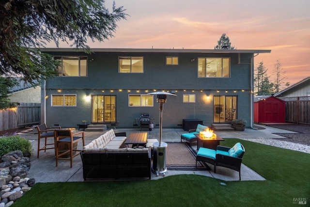 back of house at dusk with entry steps, a storage shed, an outdoor living space with a fire pit, an outdoor structure, and a patio area