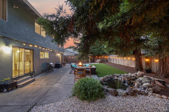 patio terrace at dusk featuring entry steps, a fenced backyard, a yard, and grilling area