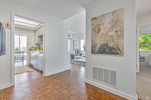 corridor featuring ornamental molding, a healthy amount of sunlight, visible vents, and baseboards