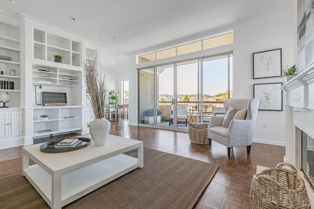 living room with ornamental molding, built in shelves, a glass covered fireplace, and baseboards