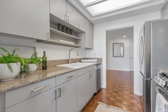 kitchen featuring a skylight, open shelves, stainless steel appliances, a sink, and light stone countertops