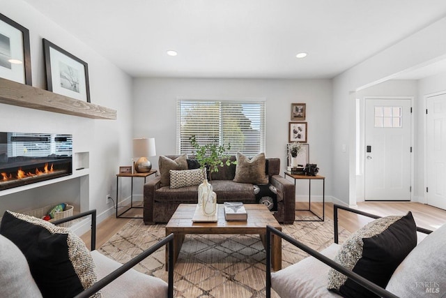 living room featuring light wood-style flooring, recessed lighting, a glass covered fireplace, and baseboards