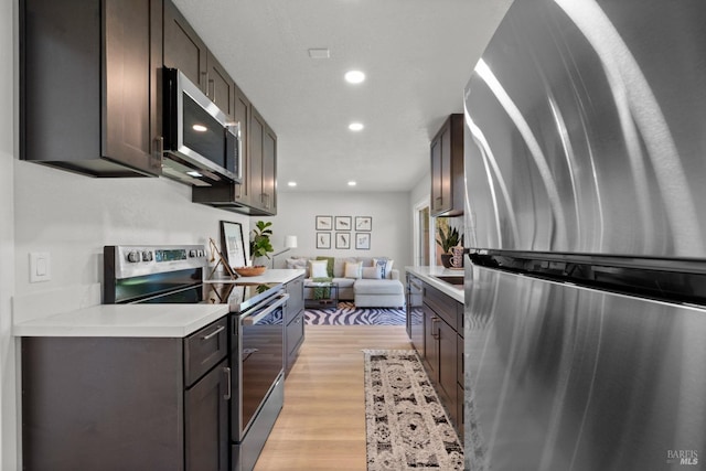kitchen featuring recessed lighting, light countertops, dark brown cabinets, light wood-type flooring, and appliances with stainless steel finishes