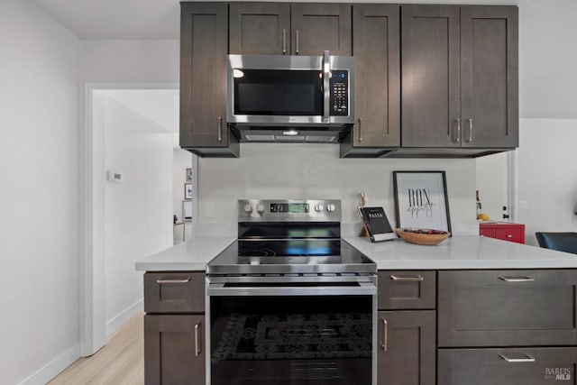 kitchen featuring baseboards, light countertops, light wood-style floors, dark brown cabinets, and stainless steel appliances
