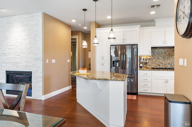 kitchen featuring dark stone counters, decorative light fixtures, a stone fireplace, white cabinetry, and stainless steel refrigerator with ice dispenser