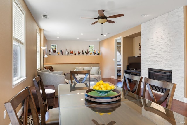 dining room with visible vents, a ceiling fan, wood finished floors, a stone fireplace, and recessed lighting