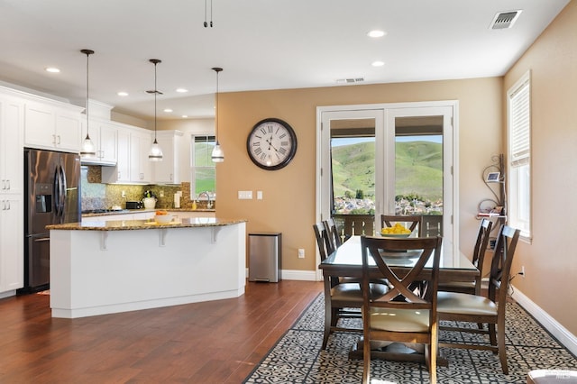 interior space featuring a breakfast bar area, decorative light fixtures, stone counters, white cabinetry, and stainless steel refrigerator with ice dispenser