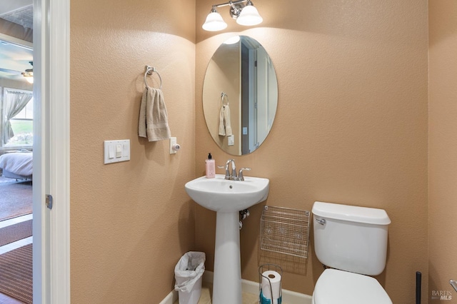 bathroom featuring a textured wall, a sink, ceiling fan, and toilet