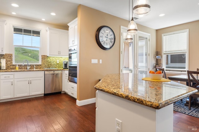 kitchen with dark wood finished floors, white cabinets, light stone counters, appliances with stainless steel finishes, and a sink