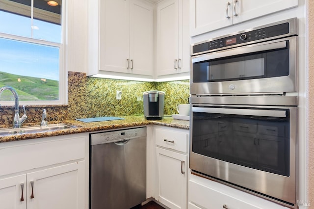 kitchen with stone countertops, white cabinets, appliances with stainless steel finishes, a sink, and backsplash