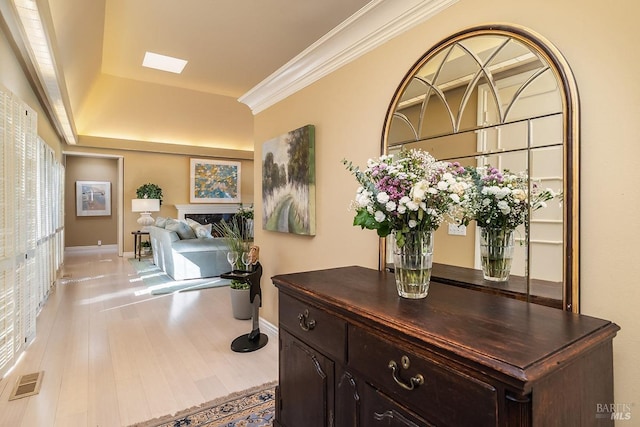 hallway featuring a skylight, baseboards, visible vents, crown molding, and light wood-style floors