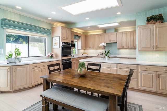 kitchen with a skylight, dobule oven black, light countertops, light brown cabinetry, and recessed lighting