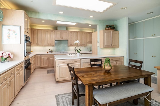 kitchen with black appliances, light brown cabinets, a skylight, and light countertops