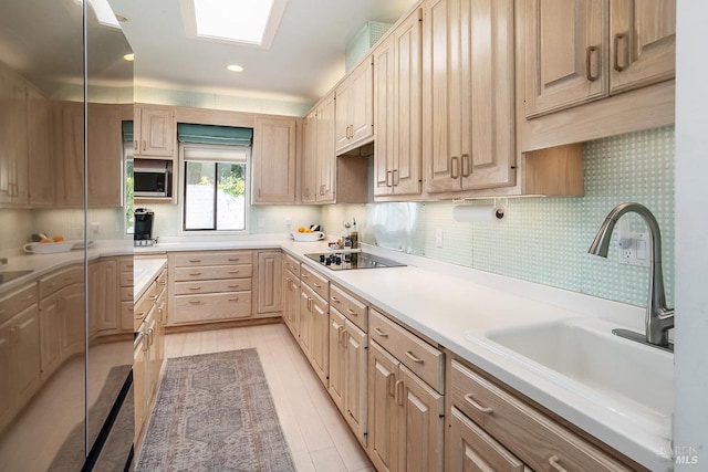 kitchen featuring black electric stovetop, light countertops, stainless steel microwave, light brown cabinets, and a sink