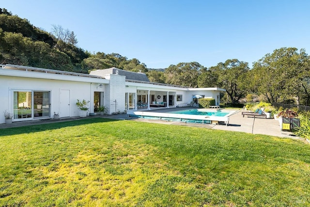 rear view of property featuring an outdoor pool, a lawn, and a patio