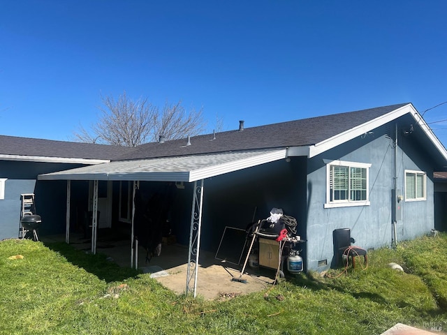 rear view of property with a shingled roof, a carport, and a yard