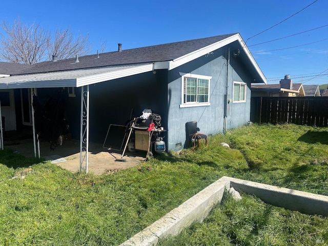 exterior space featuring a shingled roof, a patio, an attached carport, fence, and a yard