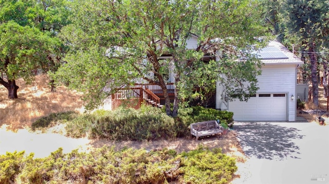 view of property hidden behind natural elements featuring solar panels, stairway, concrete driveway, and a wooden deck