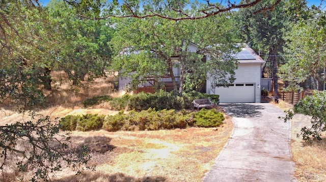 view of property hidden behind natural elements featuring driveway, a garage, and solar panels