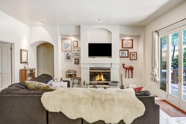 living area with light tile patterned floors, french doors, arched walkways, and a glass covered fireplace