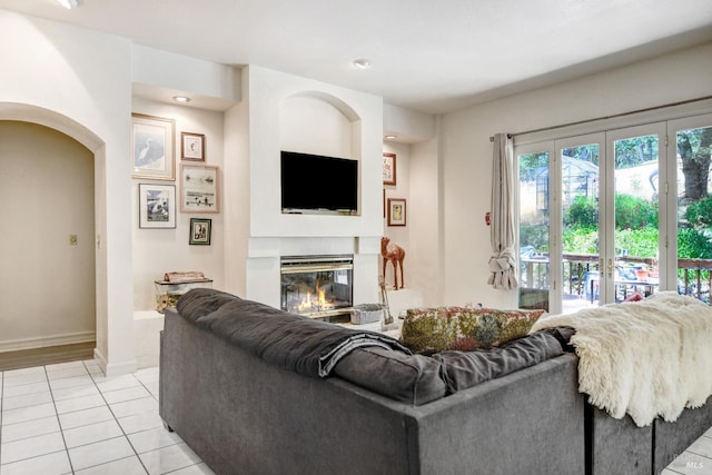 living room with a glass covered fireplace, light tile patterned flooring, arched walkways, and baseboards