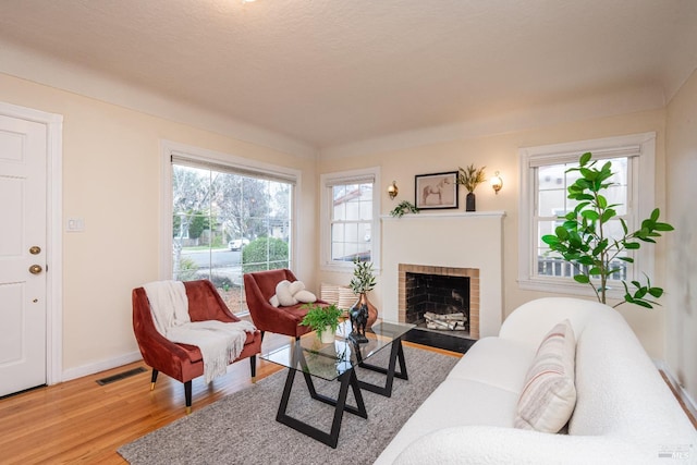 living area with baseboards, a brick fireplace, visible vents, and light wood-style floors