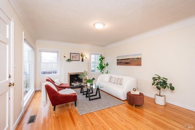 living room featuring baseboards, visible vents, wood finished floors, a textured ceiling, and a fireplace