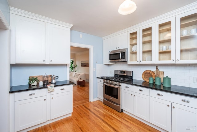 kitchen with appliances with stainless steel finishes, white cabinets, light wood-style floors, and backsplash