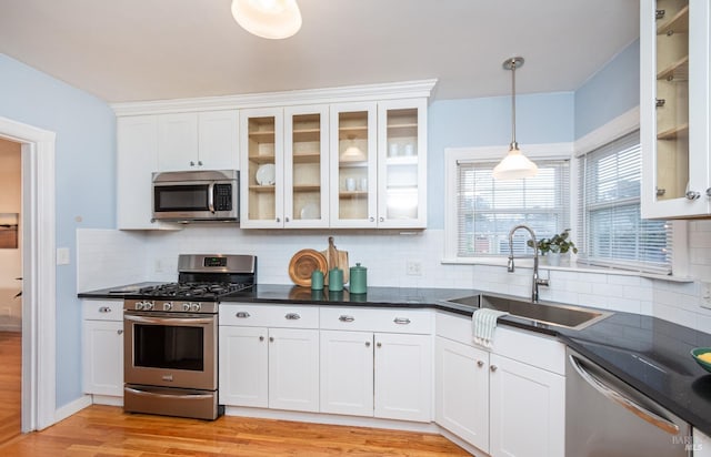 kitchen featuring white cabinets, dark countertops, appliances with stainless steel finishes, light wood-style floors, and a sink