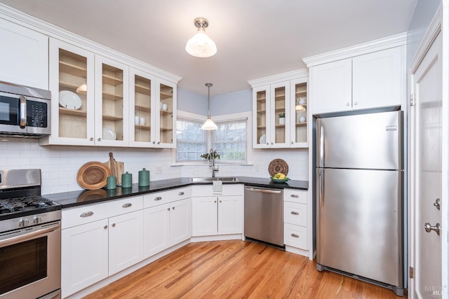 kitchen featuring light wood-style flooring, stainless steel appliances, a sink, white cabinets, and dark countertops