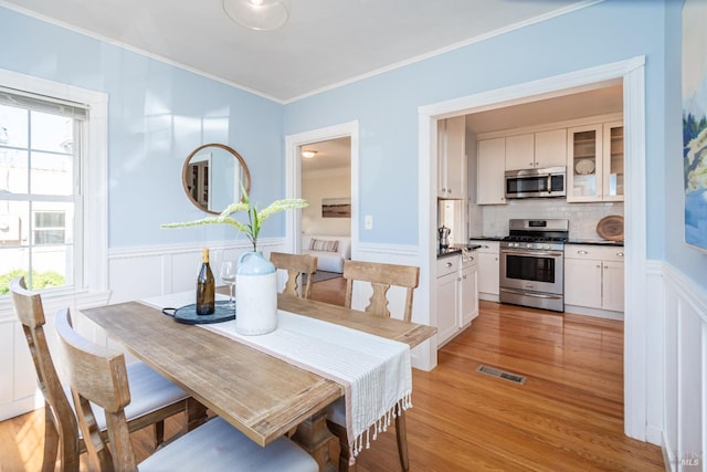 dining room with ornamental molding, light wood-type flooring, wainscoting, and visible vents