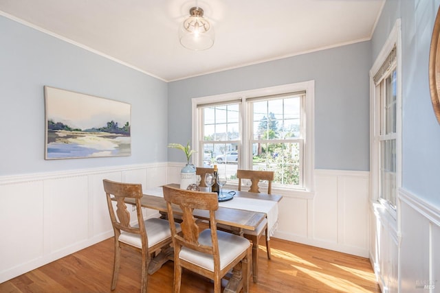 dining area with a wainscoted wall, light wood finished floors, and crown molding