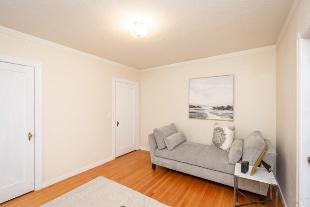 living area with crown molding, light wood-style flooring, baseboards, and a textured ceiling