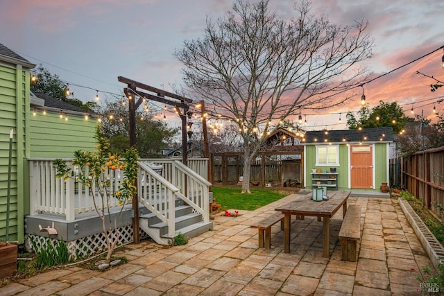 patio terrace at dusk featuring a fenced backyard, an outdoor structure, a deck, and a shed