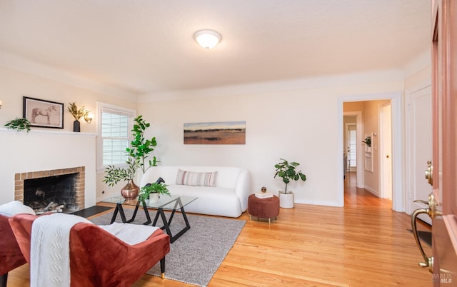 living area featuring a brick fireplace, baseboards, and wood finished floors