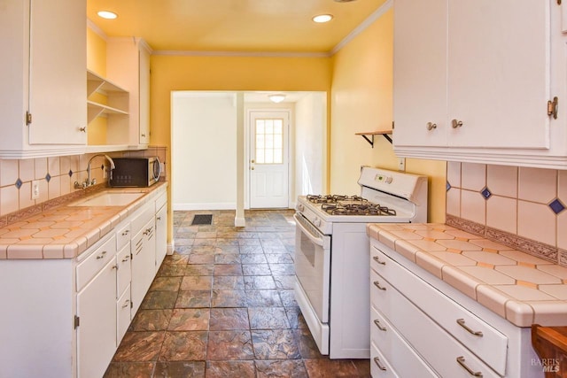 kitchen with open shelves, tile counters, white cabinets, white range with gas cooktop, and a sink