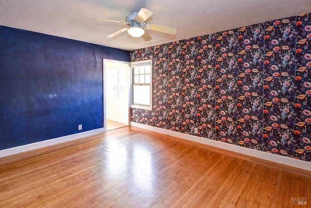 empty room with wood finished floors, a ceiling fan, and baseboards