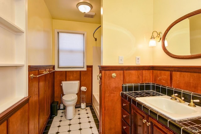 bathroom featuring a wainscoted wall, wood walls, vanity, and toilet