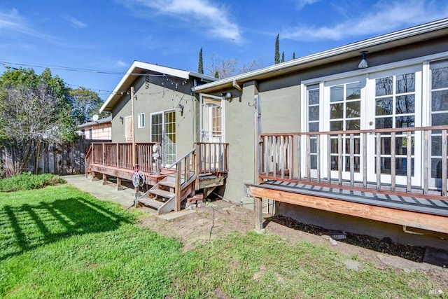 rear view of property featuring a yard, a deck, and stucco siding