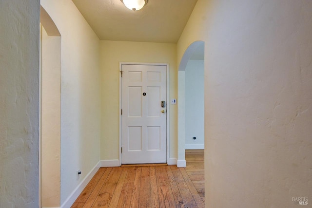 hall with light wood finished floors, baseboards, and arched walkways