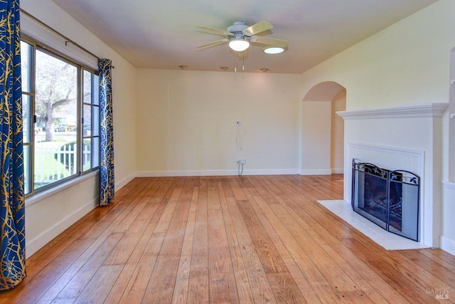 unfurnished living room with light wood-style floors, a fireplace with flush hearth, baseboards, and ceiling fan