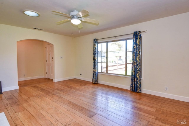 empty room with arched walkways, light wood finished floors, visible vents, a ceiling fan, and baseboards