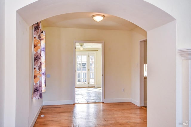 empty room with arched walkways, baseboards, and light wood finished floors