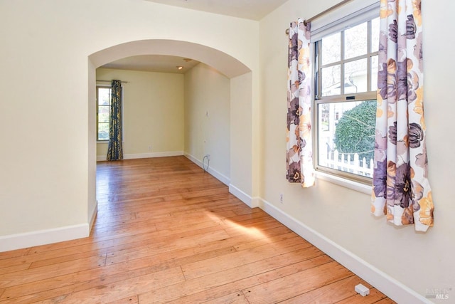 empty room featuring a healthy amount of sunlight, light wood-type flooring, arched walkways, and baseboards