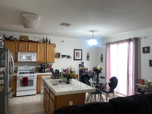 kitchen with white appliances, visible vents, tile counters, a kitchen island, and a sink