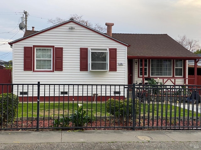 view of front facade featuring a shingled roof and a fenced front yard